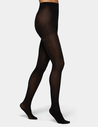 Black sheer tights worn on a model's legs, shown from the waist down against a light gray studio background.